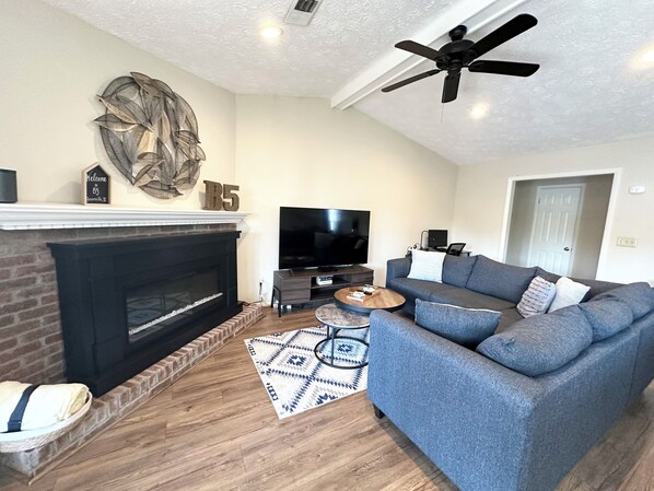 Una sala de estar con chimenea, ventilador de techo, sofá y televisor.