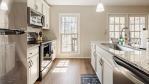 Eine Küche mit weißen Schränken, einem Edelstahlkühlschrank, einem Einbauofen, einer Mikrowelle, einem Spülbecken und einem Fenster, das für natürliches Licht sorgt.