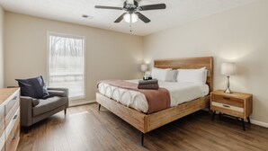 Ein Schlafzimmer mit einem Holzbett, einem Nachttisch, einem Stuhl, einem Deckenventilator und einem Fenster mit Jalousien.