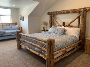 Un lit en bois rustique, sous un plafond en pente, avec une fenêtre.