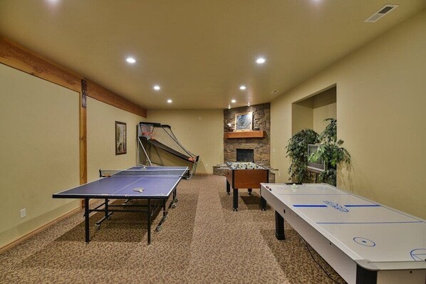 Une pièce équipée d’une table de ping-pong, d’un baby-foot et d’un autre baby-foot, avec un mur en pierre et une cheminée.