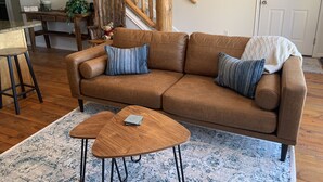 Un sofá de cuero marrón con dos almohadas, una mesa de centro de madera y una escalera con barandillas de madera.