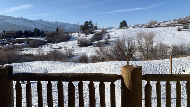 Paisaje nevado con montañas al fondo, una cerca de madera en primer plano y un cielo azul despejado.