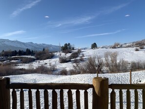 Un paysage enneigé avec des montagnes en arrière-plan, une clôture en bois au premier plan et un ciel bleu dégagé.