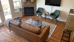 Una sala de estar con un sofá de cuero marrón, una chimenea de piedra, un televisor montado y dos sillones verdes.