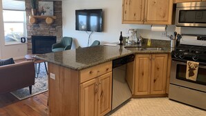 Una cocina moderna con armarios de madera, una pared decorativa de piedra, un televisor de pantalla plana, una cafetera y un horno de acero inoxidable.