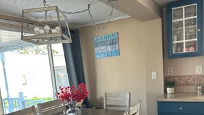 A dining area with a wooden table, chairs, a vase with red flowers, a ceiling light fixture, and a kitchen with blue cabinets. - Spacious Cottage Close to Beach (Lexington)