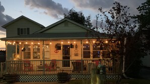 A house with a porch decorated with string lights, a small American flag, and a wooden post with a rope. - Spacious Cottage Close to Beach (Lexington)