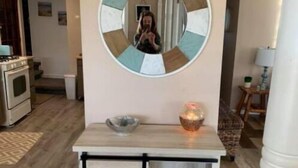 A kitchen area with a wooden cabinet, a round mirror, and a small table with a bowl and candle. - Spacious Cottage Close to Beach (Lexington)
