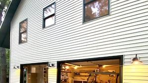 A two-story house with a garage open to the street, revealing bicycles and a golf cart inside. - Luxury Guesthouse in private wooded setting in Grand Beach New Buffalo (New Buffalo)