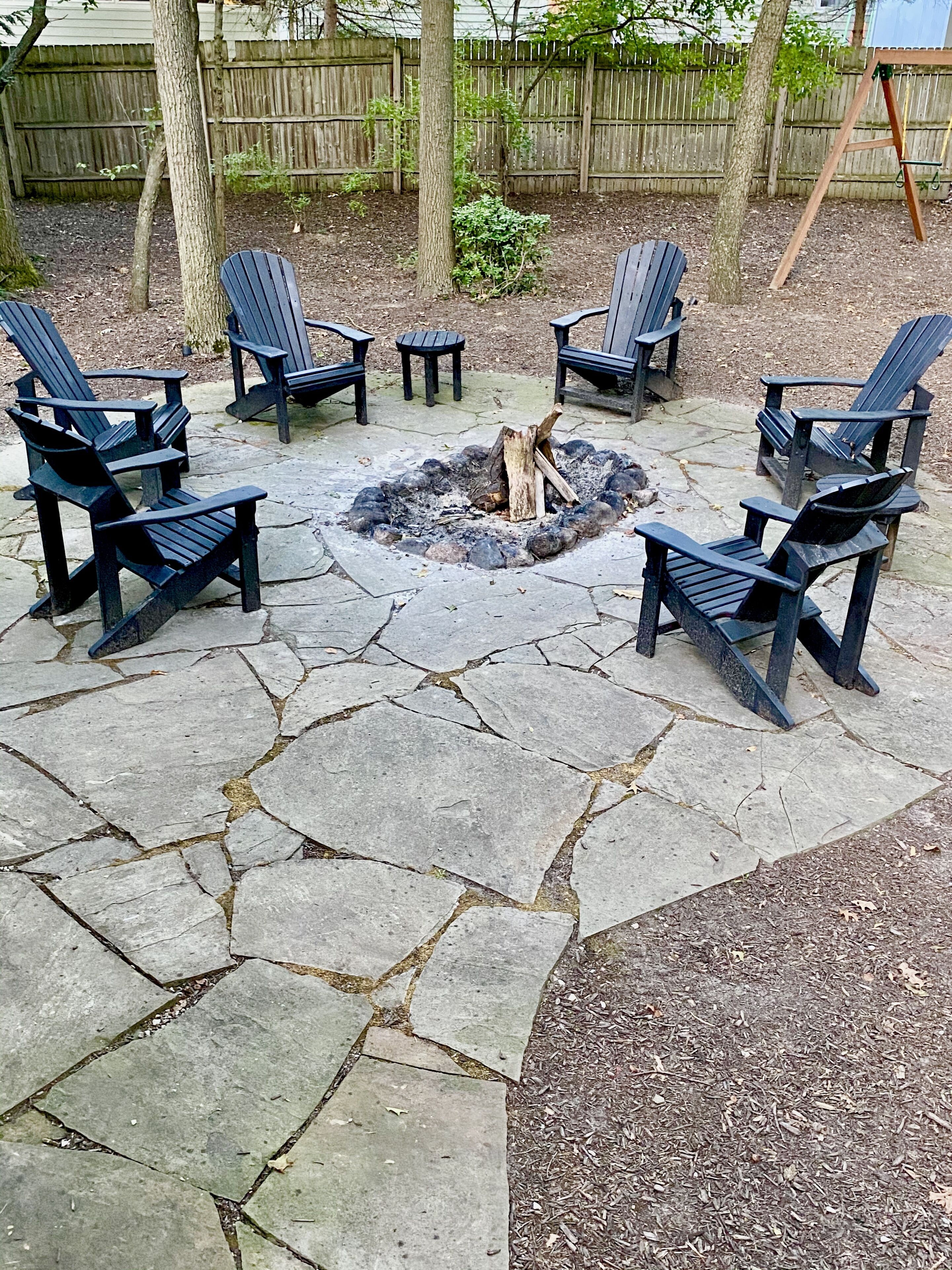 Een terras van stenen met Adirondack stoelen rond een vuurkuil.