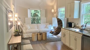 A modern kitchen with a central island, a dining area with a white sofa, and a ceiling fan. - Luxury Guesthouse in private wooded setting in Grand Beach New Buffalo (New Buffalo)