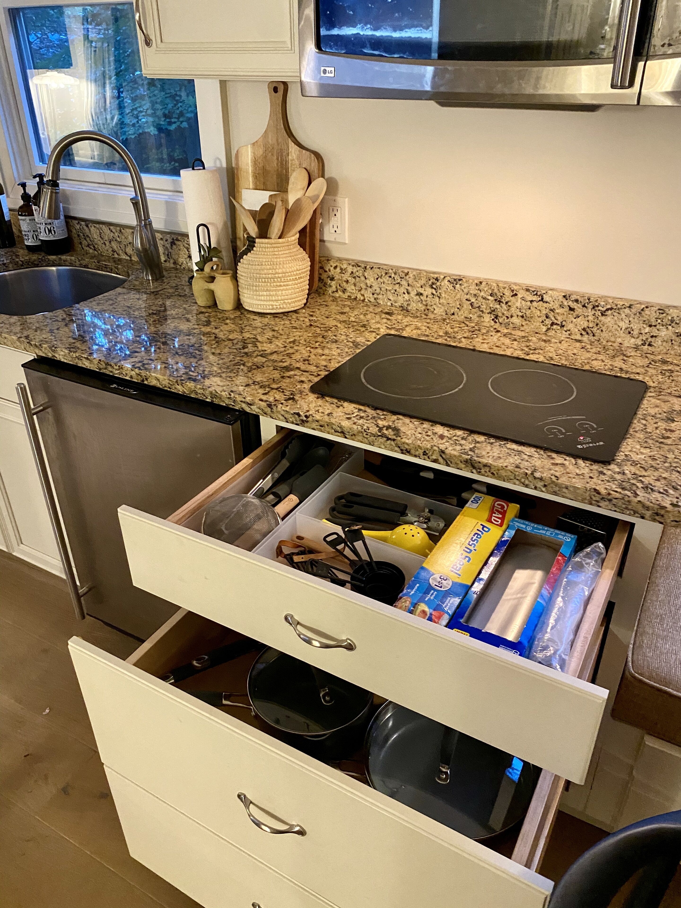 A kitchen with a built-in microwave, a stainless steel dishwasher, and a drawer with kitchen utensils and packaged food items.