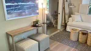 A cozy living room with a wooden floor, a large abstract painting, a white sofa, and a small table with two ottomans. - Luxury Guesthouse in private wooded setting in Grand Beach New Buffalo (New Buffalo)