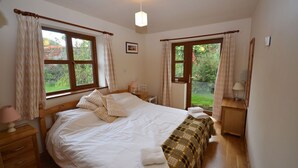 A bedroom with a large bed, two bedside tables, a nightstand, a lamp, and a window with curtains.