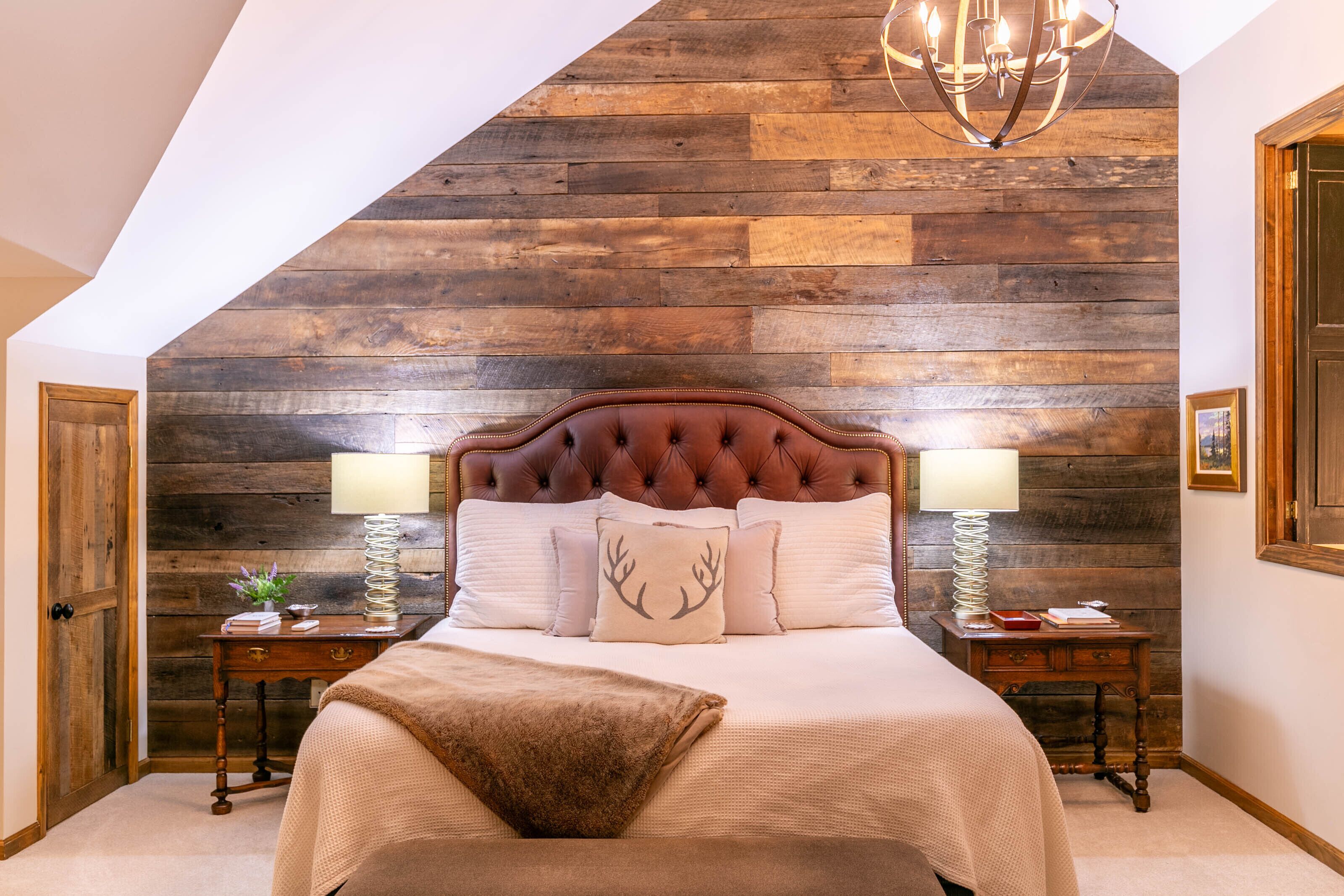 A bedroom with a wooden slat ceiling, a tufted headboard, two bedside tables with lamps, and a bed with a decorative pillow.