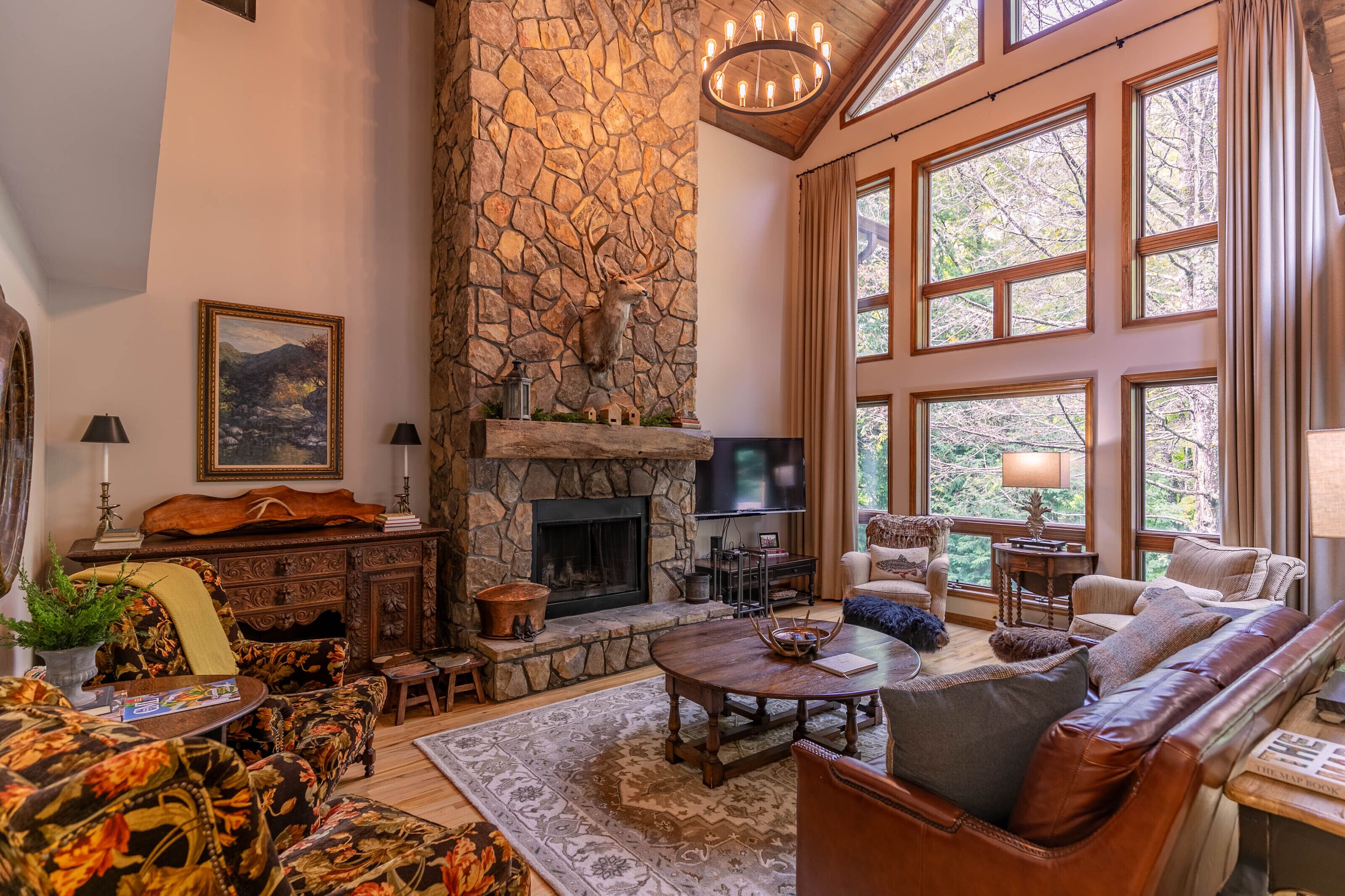 A cozy living room with a stone fireplace, large windows, and comfortable seating.