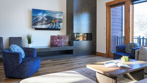 Una sala de estar moderna con chimenea, asientos cómodos, televisor y vistas al exterior.