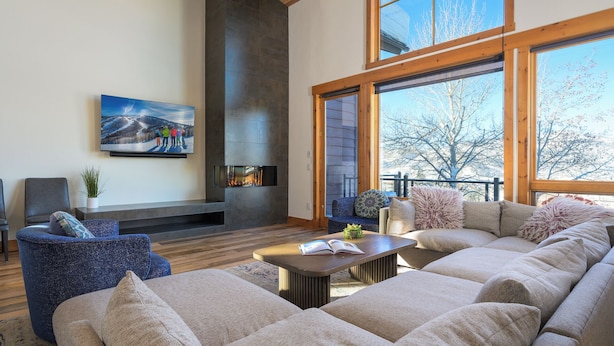 Un salón amplio con un sofá seccional grande, una chimenea y ventanas grandes que ofrecen vistas al exterior.