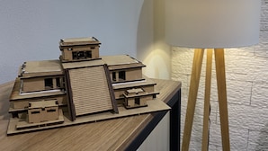 A model of a building with multiple levels and a sloped roof, displayed on a wooden table next to a lamp with a white shade. - Beautiful and comfortable apartment in the Mayan jungle.  (Tulum)