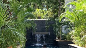 A swimming pool with a waterfall feature surrounded by lush greenery and modern architecture. - Beautiful and comfortable apartment in the Mayan jungle.  (Tulum)
