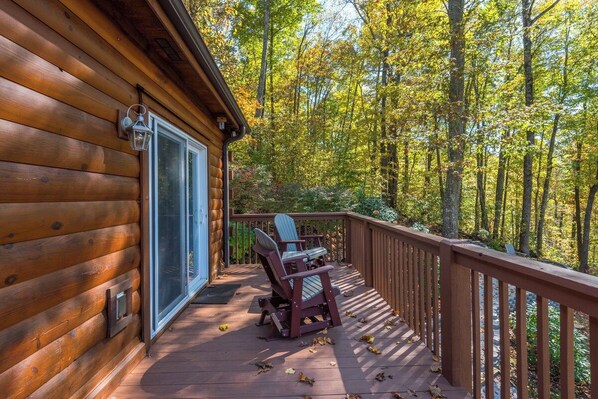 Een houten chalet met een terras, een stoel en een raam.