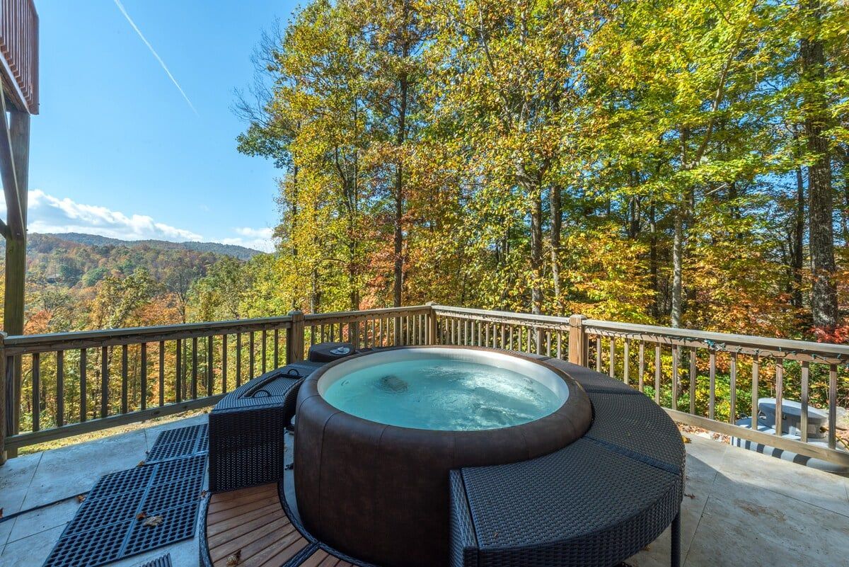 Un jacuzzi en una terraza de madera con vistas a árboles otoñales y una montaña al fondo.