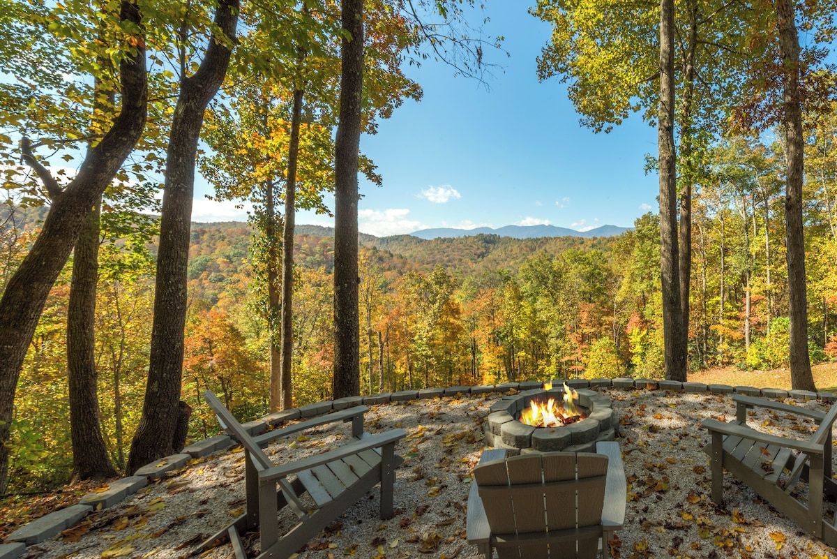 A circular outdoor seating area with a fire pit, surrounded by trees and a view of a mountainous landscape.