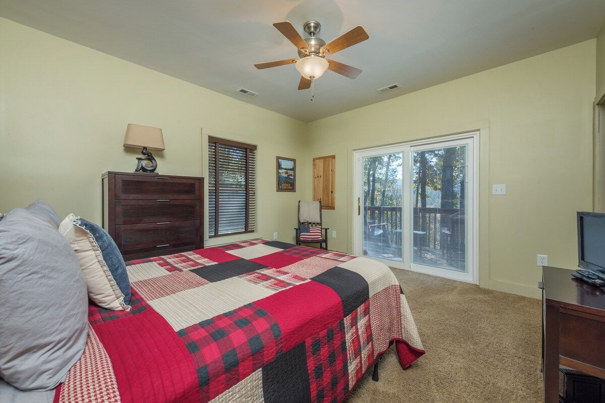 A bedroom with a bed, a dresser, a ceiling fan, a window with blinds, and a door leading to a balcony.
