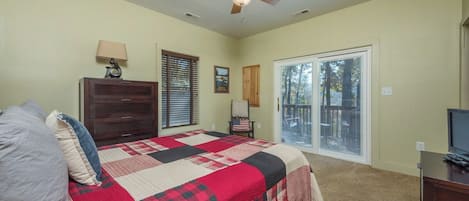 A bedroom with a bed, a dresser, a ceiling fan, a window with blinds, and a door leading to a balcony.