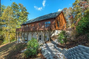 A log cabin with a balcony, surrounded by trees and a stone retaining wall. - Fire Pit & Fireplace~Mtn View~Grill & WiFi (Spruce Pine)