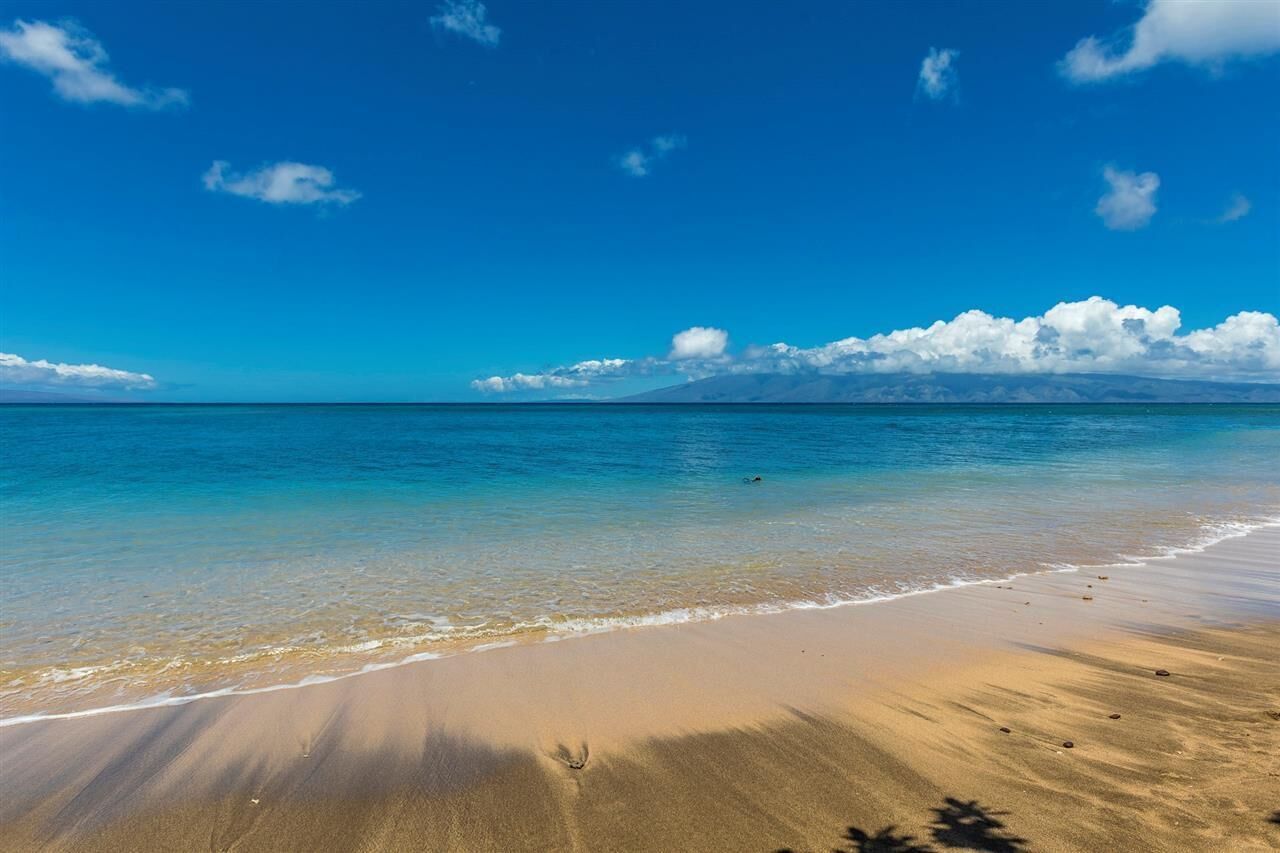 Una playa con agua azul cristalina, una orilla arenosa y una montaña al fondo.