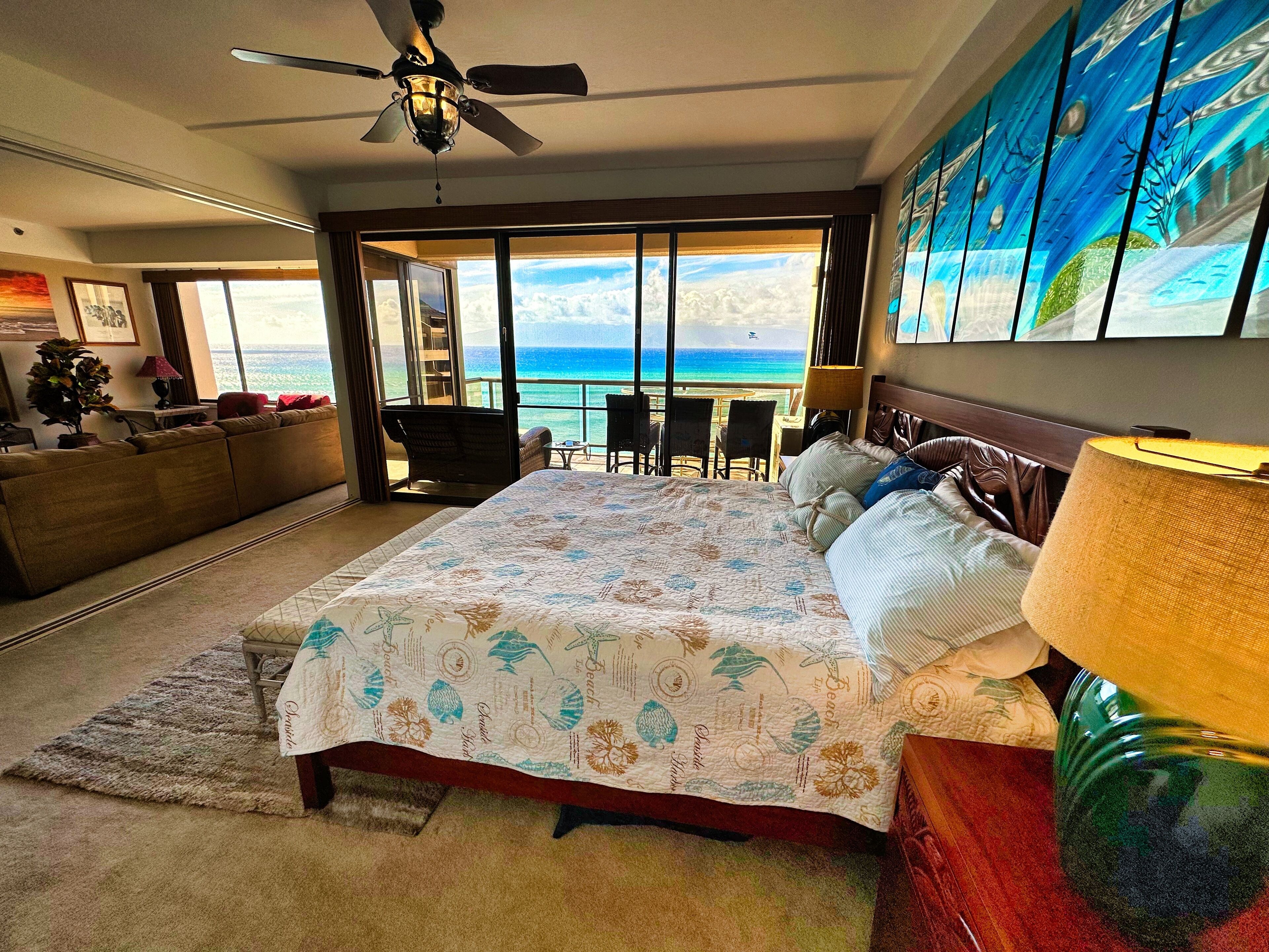 Quarto com uma cama grande, ventilador de teto, vista para o oceano e varanda com cadeiras.