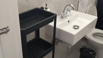 Een badkamer met een witte wastafel, een glazen plank erboven, een zwart opbergmeubel, een toilet en een zwarte prullenbak.