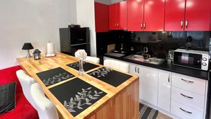 A modern kitchen with red cabinets, a wooden dining table with black placemats, and a white sofa. -  Cute & luxury suite with patio, just few steps away from beach , nearby Delphi (ΙΤΕΑ- ΚΙΡΡΑ)