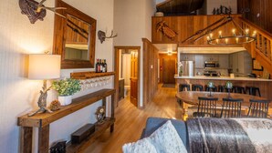 A cozy living room with a fireplace, wooden furniture, and a dining area with a chandelier. - Luxe Mountain Cabin Condo, Prime Location Between Cyn Lodge & Village, Sleeps 10 (Mammoth Lakes)