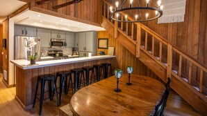 A modern kitchen with a central island, bar stools, and a wooden staircase. - Luxe Mountain Cabin Condo, Prime Location Between Cyn Lodge & Village, Sleeps 10 (Mammoth Lakes)