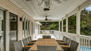 A covered outdoor deck with a wooden table and wicker chairs, overlooking a swimming pool.