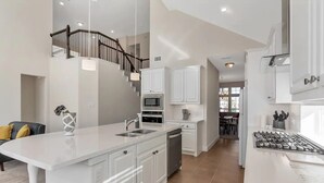 Una cocina moderna con armarios blancos, una isla central y una escalera que sube a un nivel superior.
