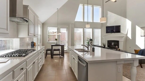 Una cocina moderna con una isla grande, armarios blancos y un ventilador de techo.