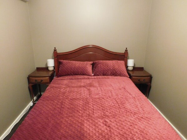 A neatly made bed with a red bedspread and two bedside lamps.