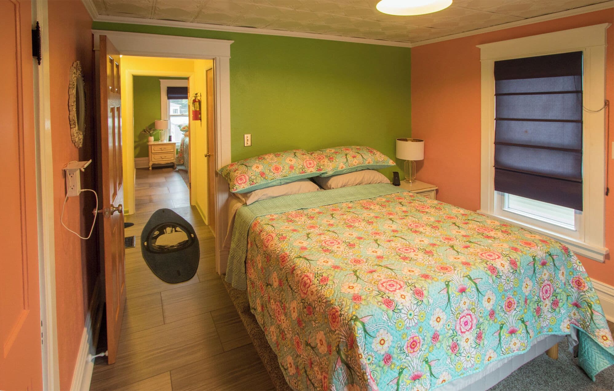 Een slaapkamer met een bloemenbedekker, een bedlampje en een raam met zonwering.
