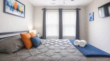 Habitación de hotel con cama, ventilador de techo, un cuadro en la pared y una ventana con cortinas.