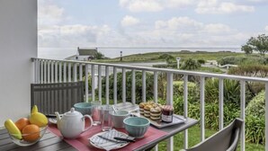 Un balcon avec une table dressée pour le petit-déjeuner, offrant une vue sur un paysage côtier.