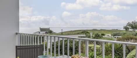 A balcony with a table set for breakfast, overlooking a coastal landscape.