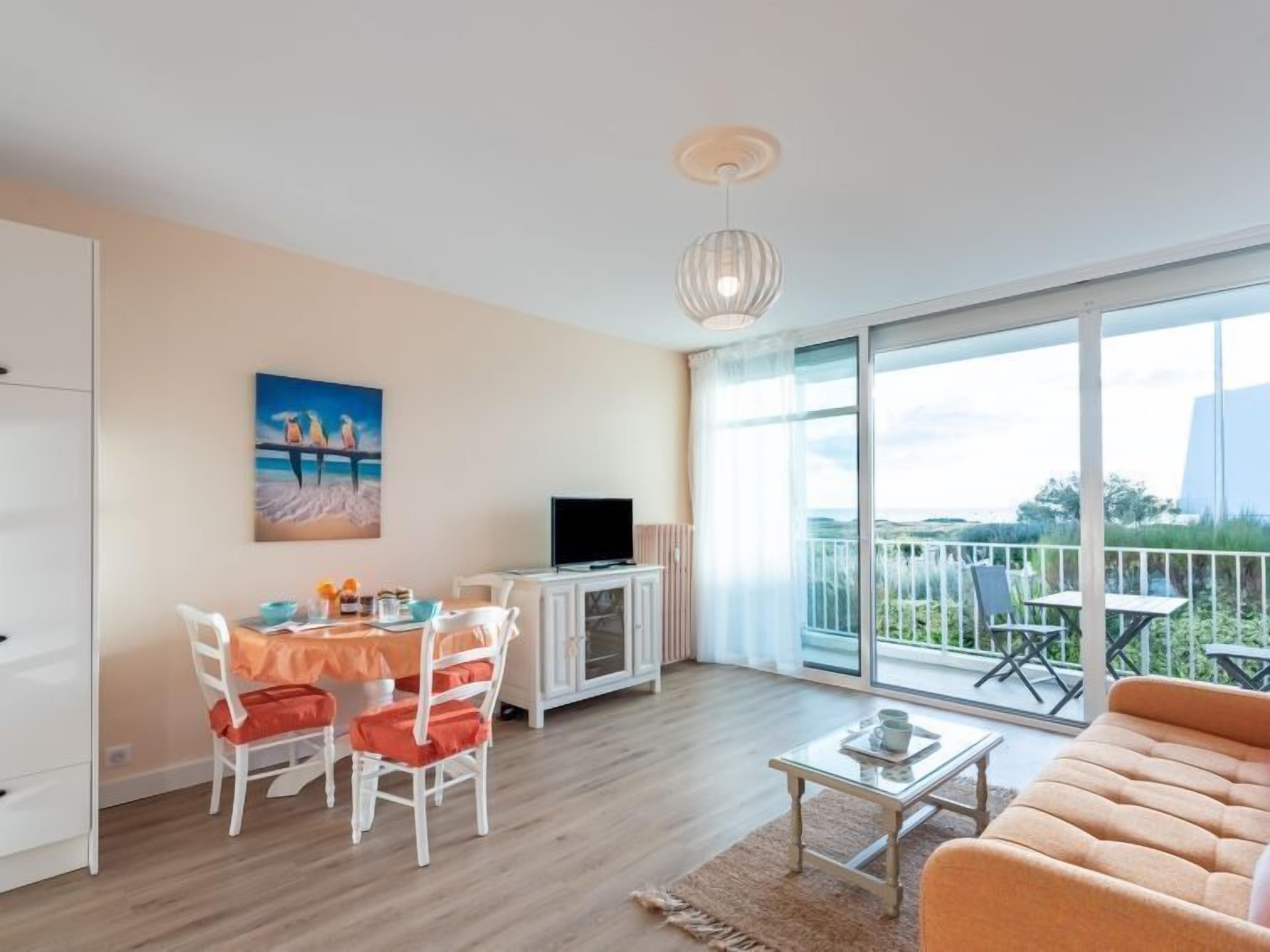 Un salon moderne comprenant un canapé, une table à manger avec des chaises, un téléviseur et un balcon offrant une vue sur le paysage.