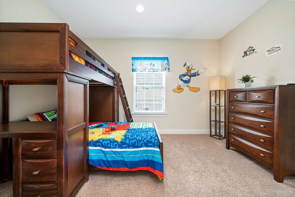 A child's bedroom with a bunk bed, a desk, a dresser, and a window with blinds.