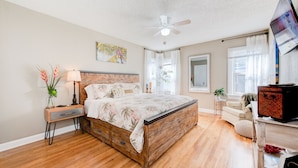 A bedroom with a wooden bed, a nightstand with a lamp, a ceiling fan, and a TV on a stand.