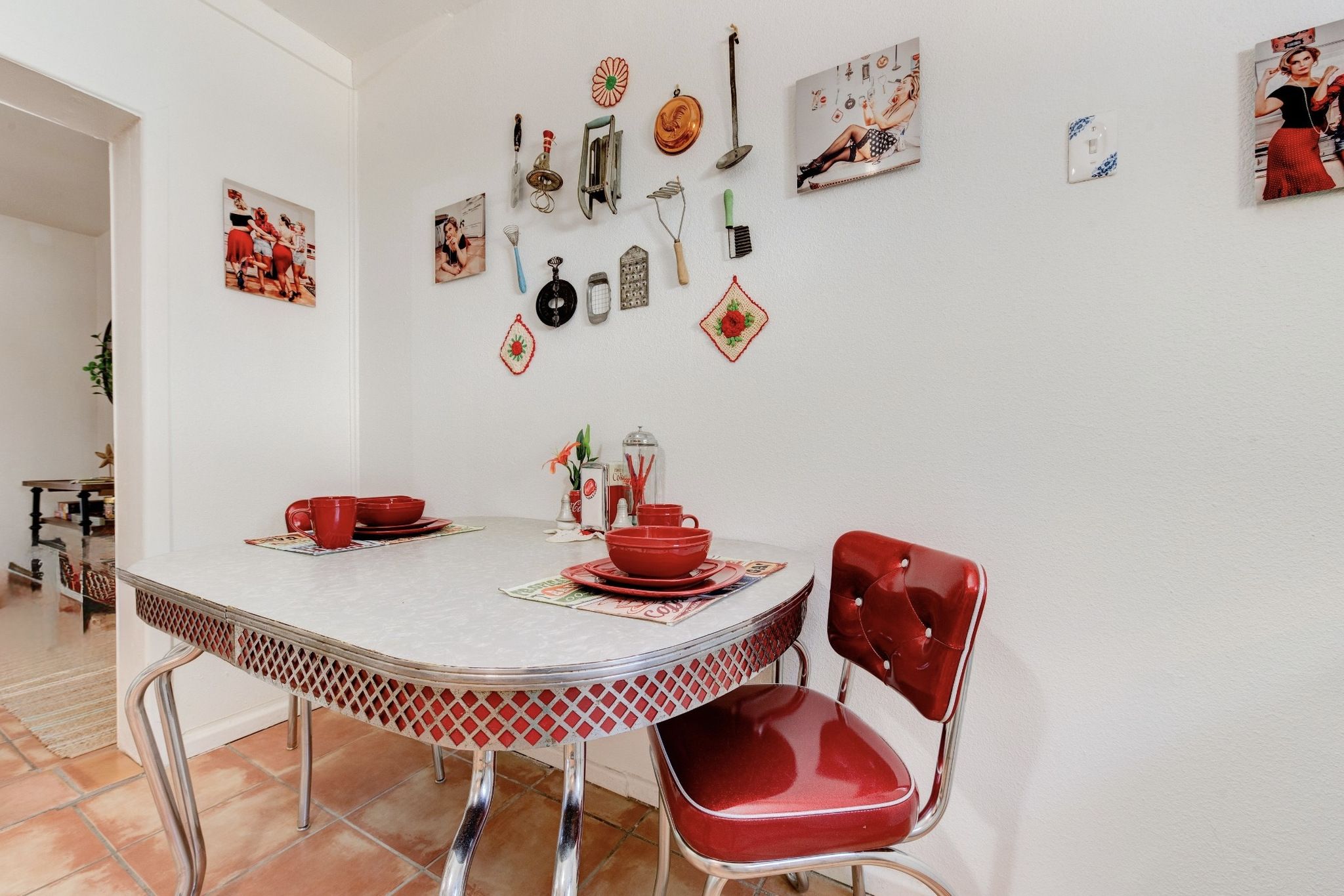 Un comedor con una mesa redonda, sillas rojas y distintos utensilios de cocina además de adornos en la pared.