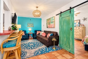 A living room with a blue wall, a brown sofa, a dining area with wicker furniture, and a green door.